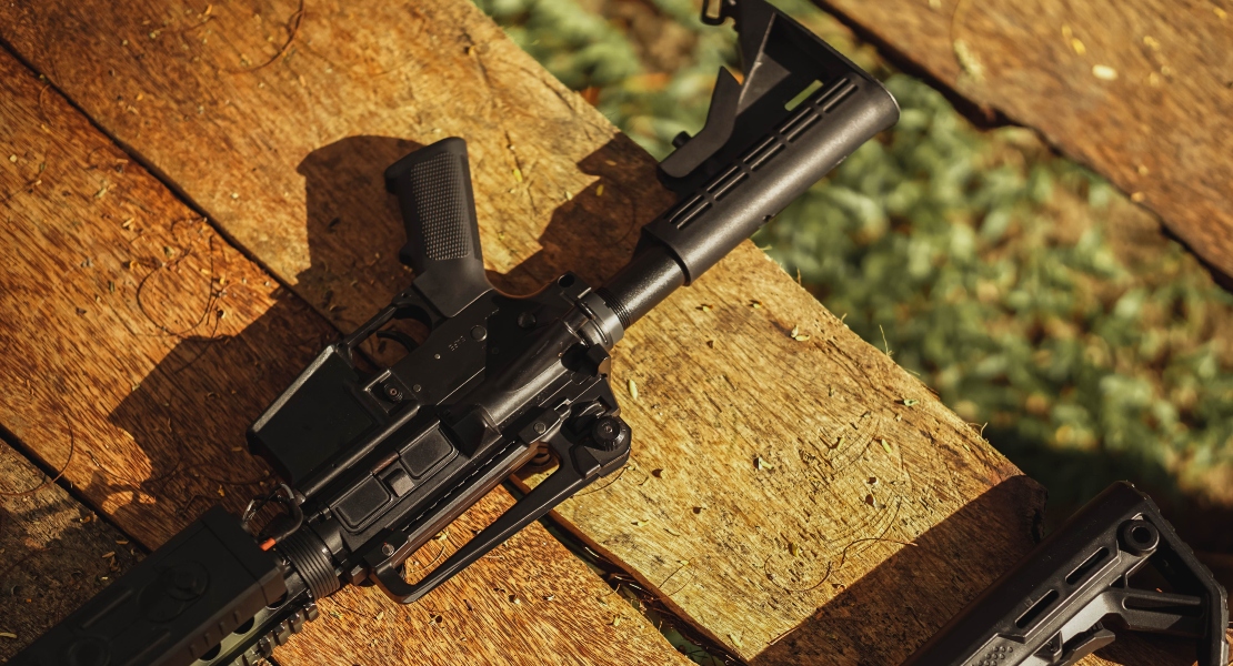 A forged AR-15 lower receiver on a gun, sitting non a wooden bench.