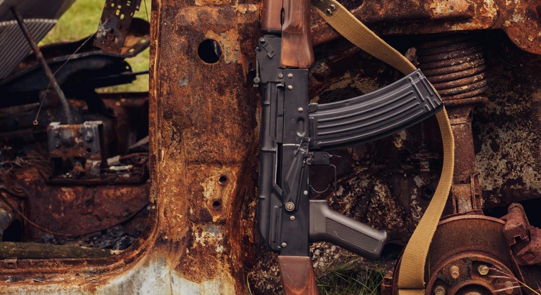 An AK leaning near a rusty damaged car