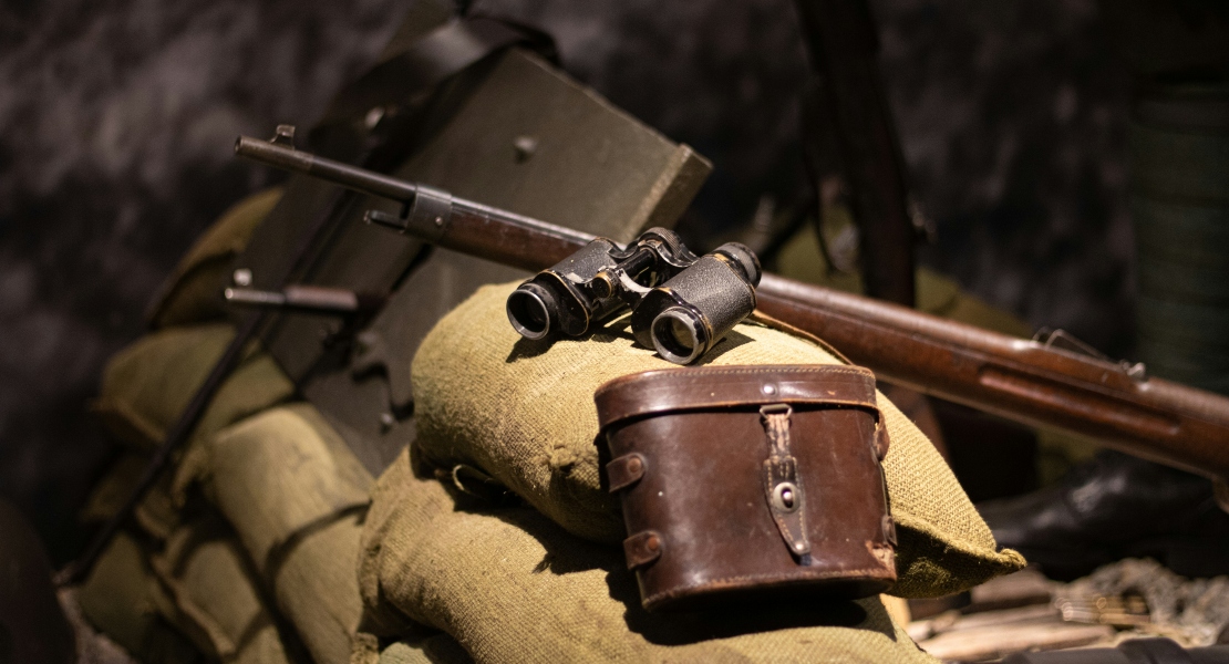 Binoculars and a rifle on top of a bag.