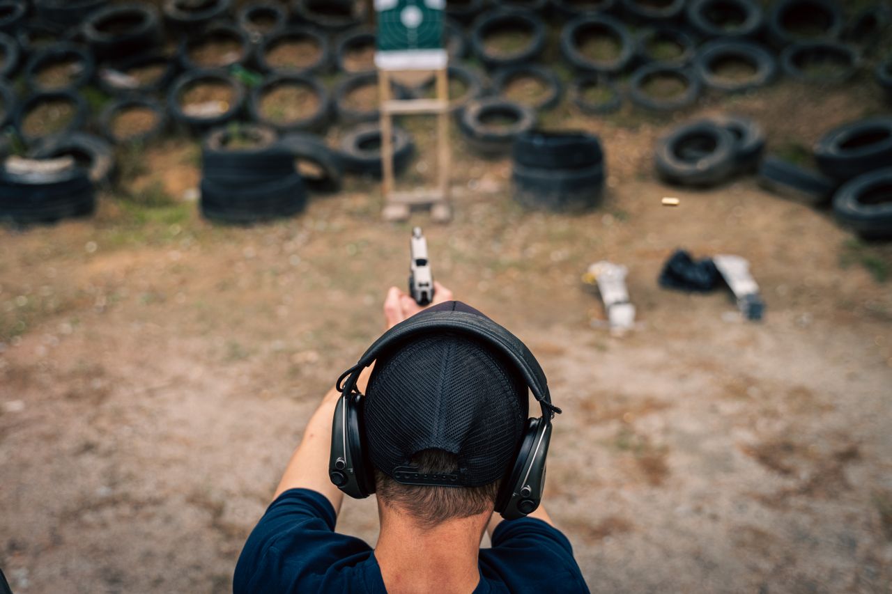 a man aiming a pistol at a target in an outdoor shooting range with headphones on