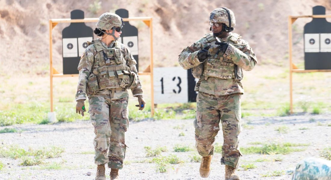 Two soldiers in military uniforms practicing at an outdoor shooting range with targets visible