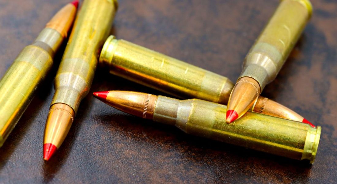 view of high-caliber rifle bullets with red tips on a textured surface