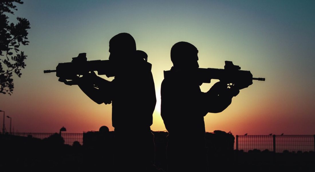 Silhouette of two civilians with rifles against a vivid sunset sky