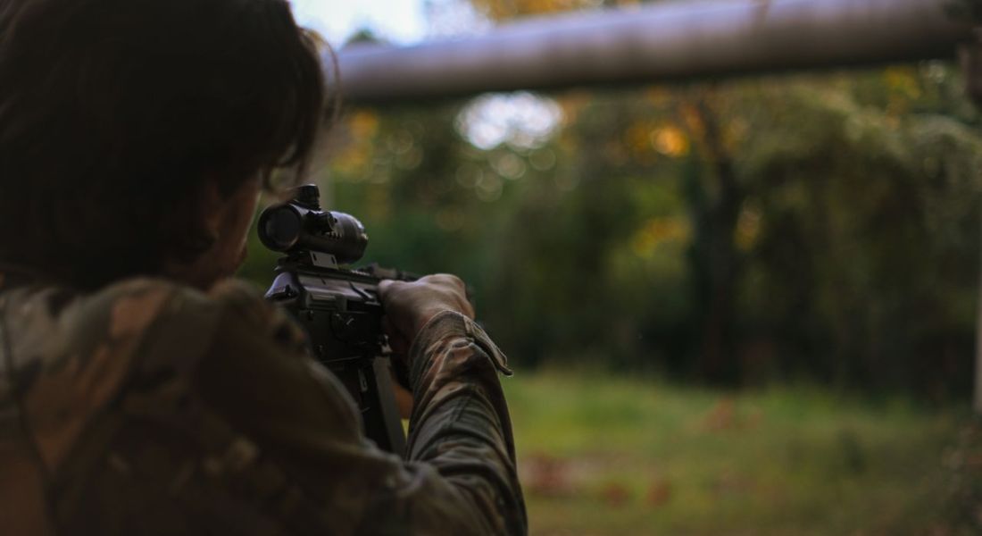 a person in camo gear aiming a gun in a wooded area