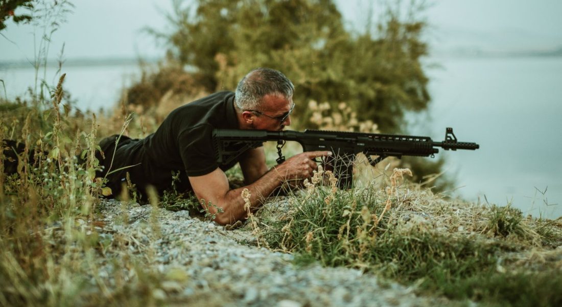 a military sniper in camouflage surveying the landscape with a rifle