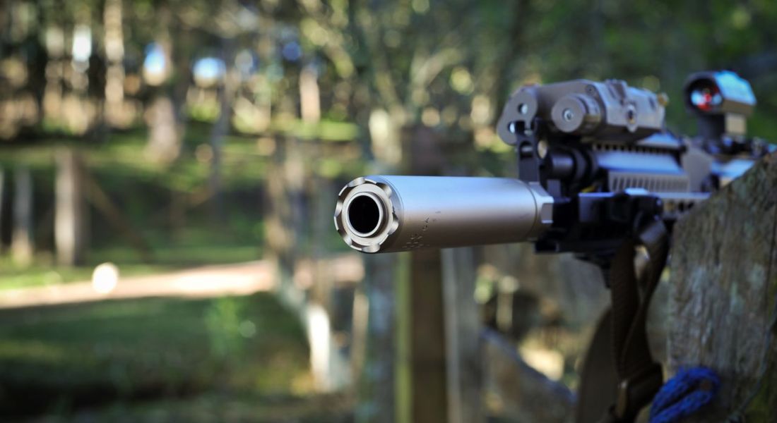 close-up of a suppressed rifle barrel outdoors in a wooded area