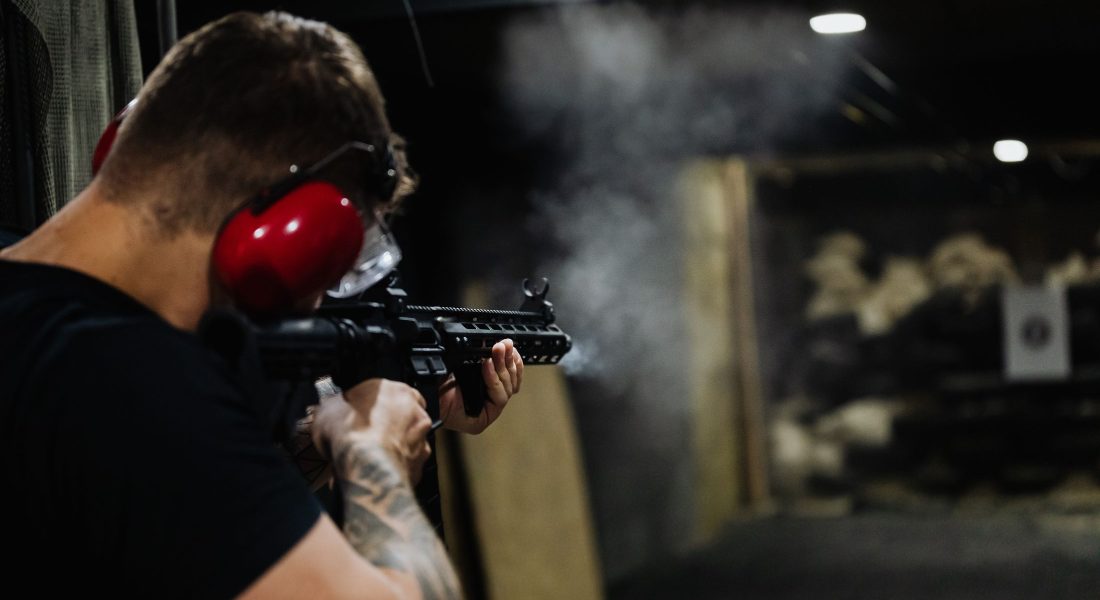 Shooter wearing red earmuffs firing a carbine at an indoor shooting range