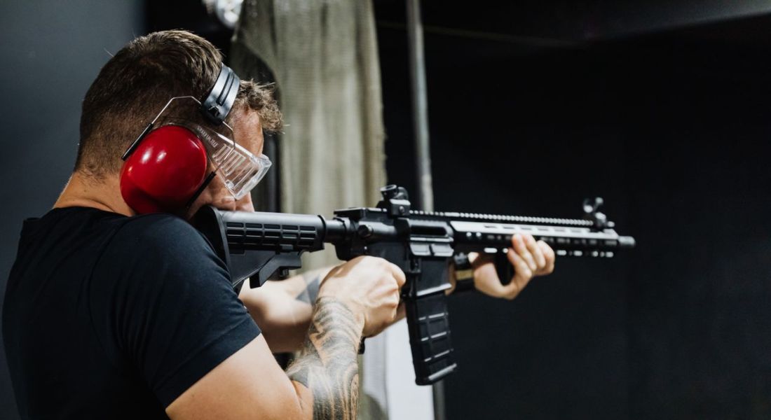 man wearing earmuffs aiming an AR-15 style rifle at an indoor shooting range