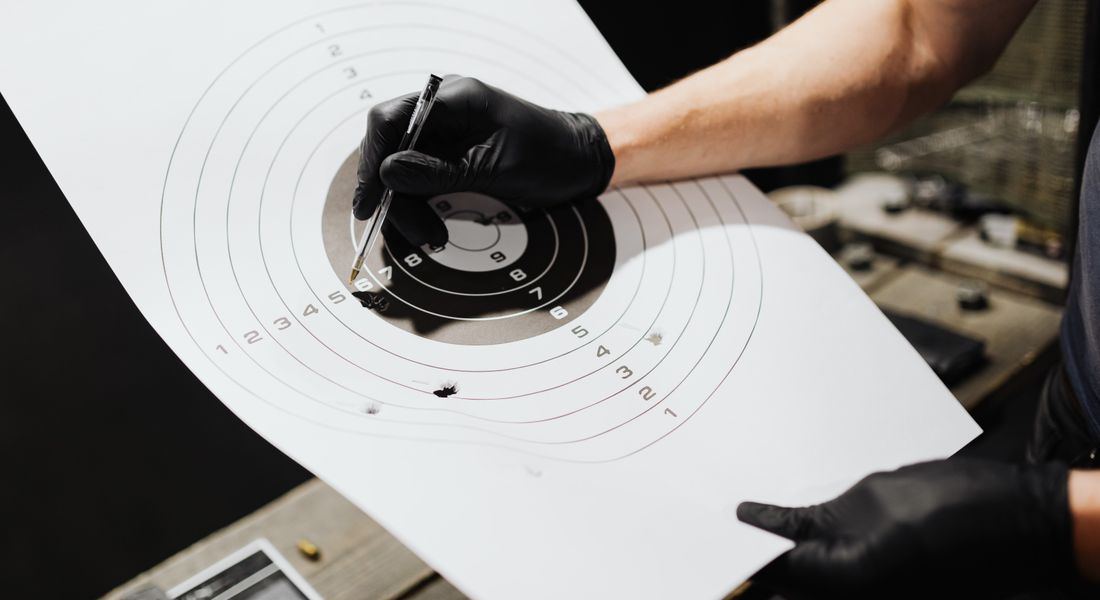 Gloved hands marking bullet holes on a paper target at a shooting range