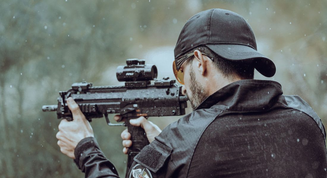Man aiming a compact carbine with a red dot sight outdoors